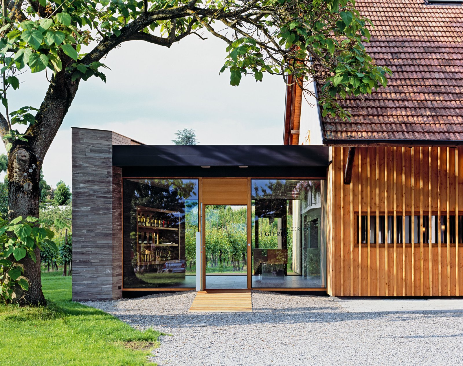 Tatsächliche Vinothek des Winzerhofs Gierer in Nonnenhorn mit Holzfassade, Reben und Weinflaschen hinter den Glasflächen.