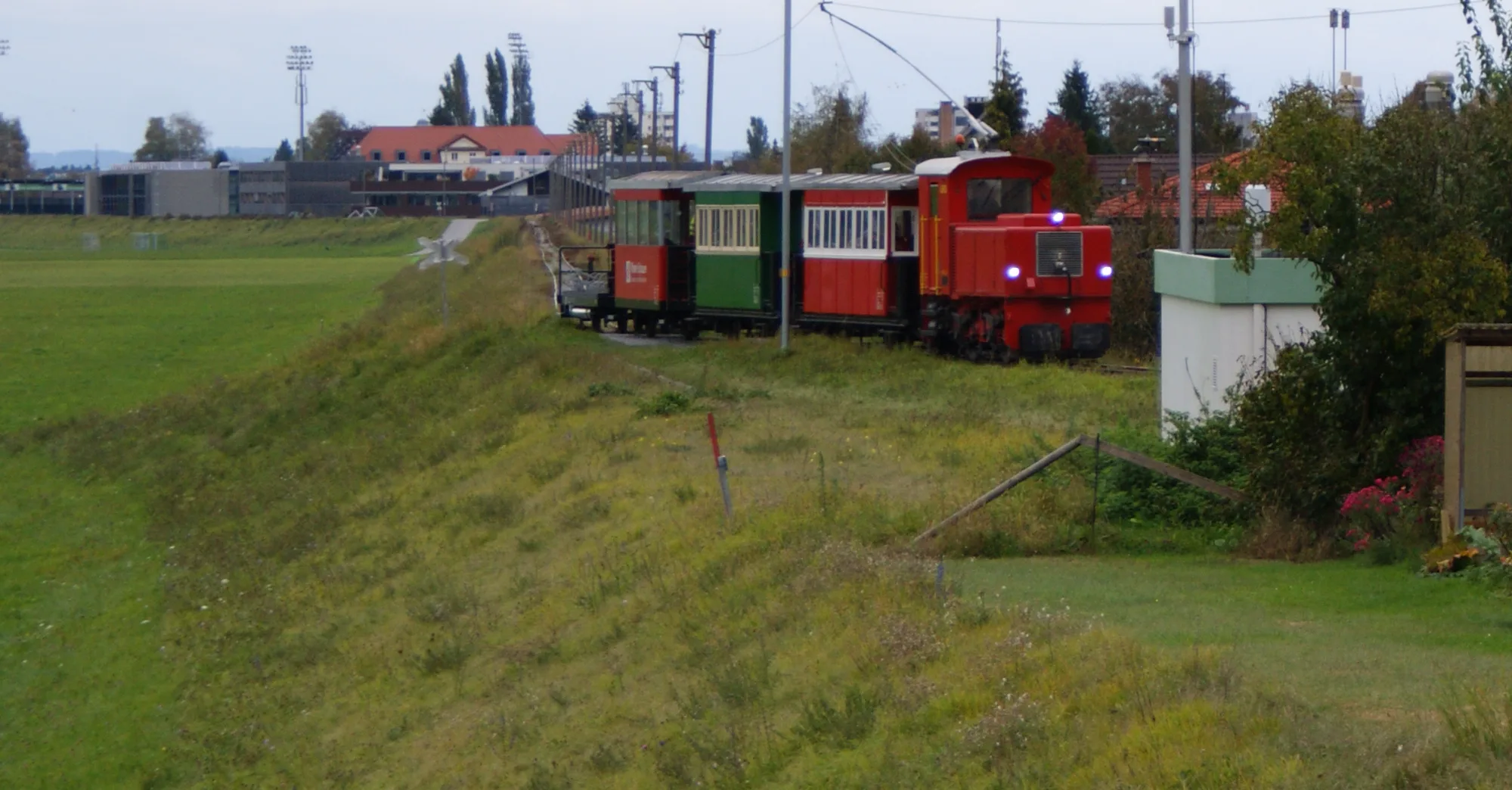 Historischer Rheinbähnle-Ausflugszug mit roter Lok Urs auf dem Rheindamm in Lustenau